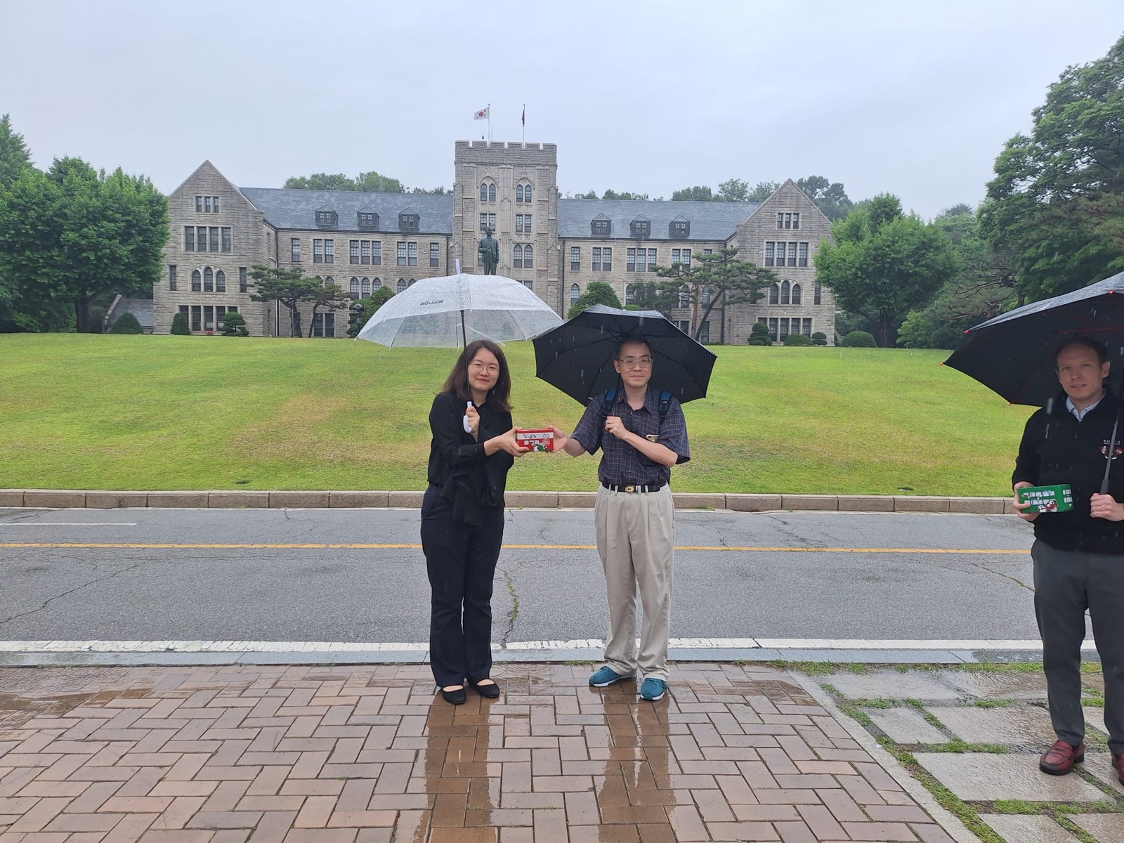 A second souvenir handover under umbrellas by the main building