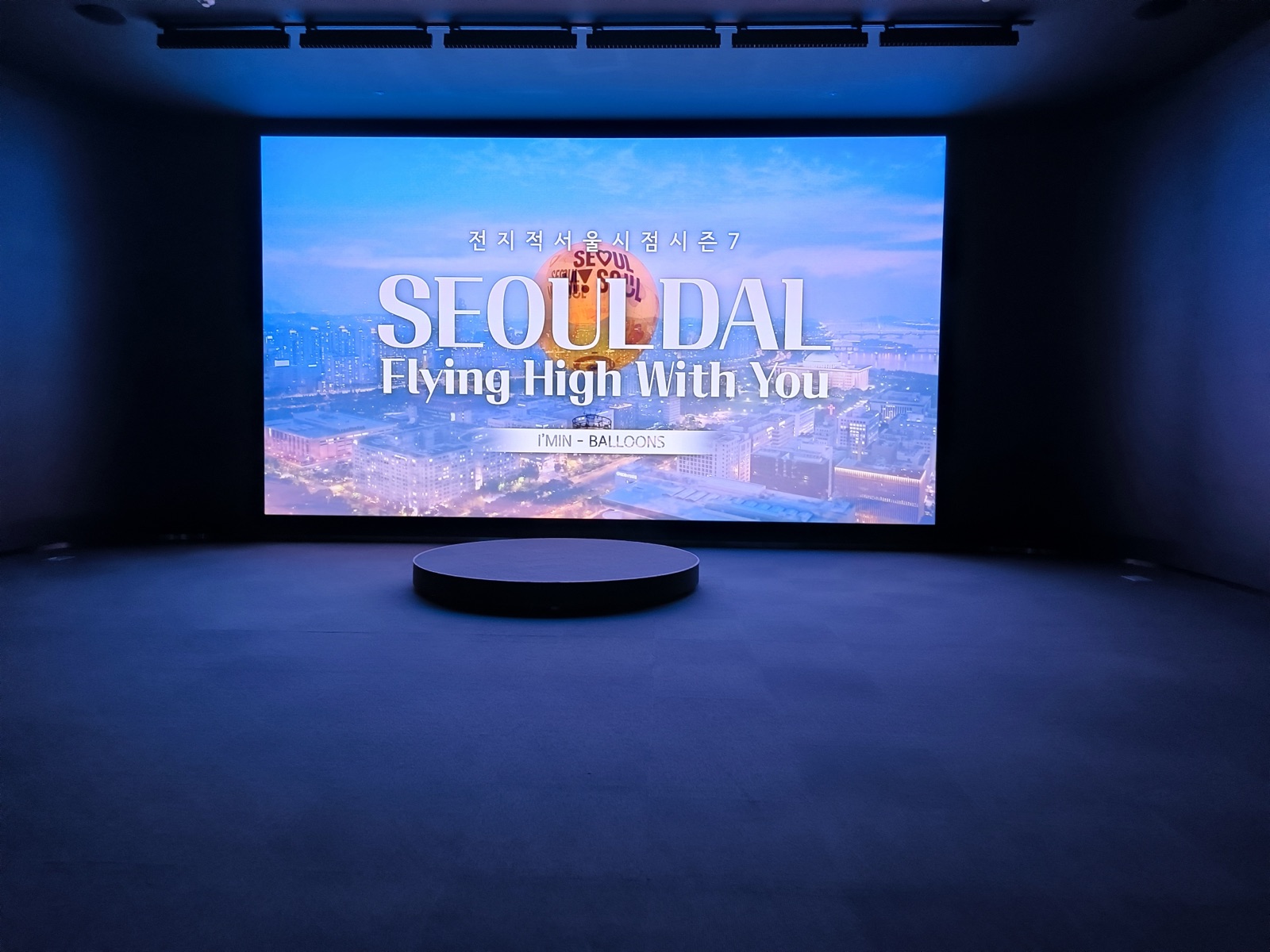 A dark immersive media room with a huge screen reading Seoul Dal — Flying High With You
