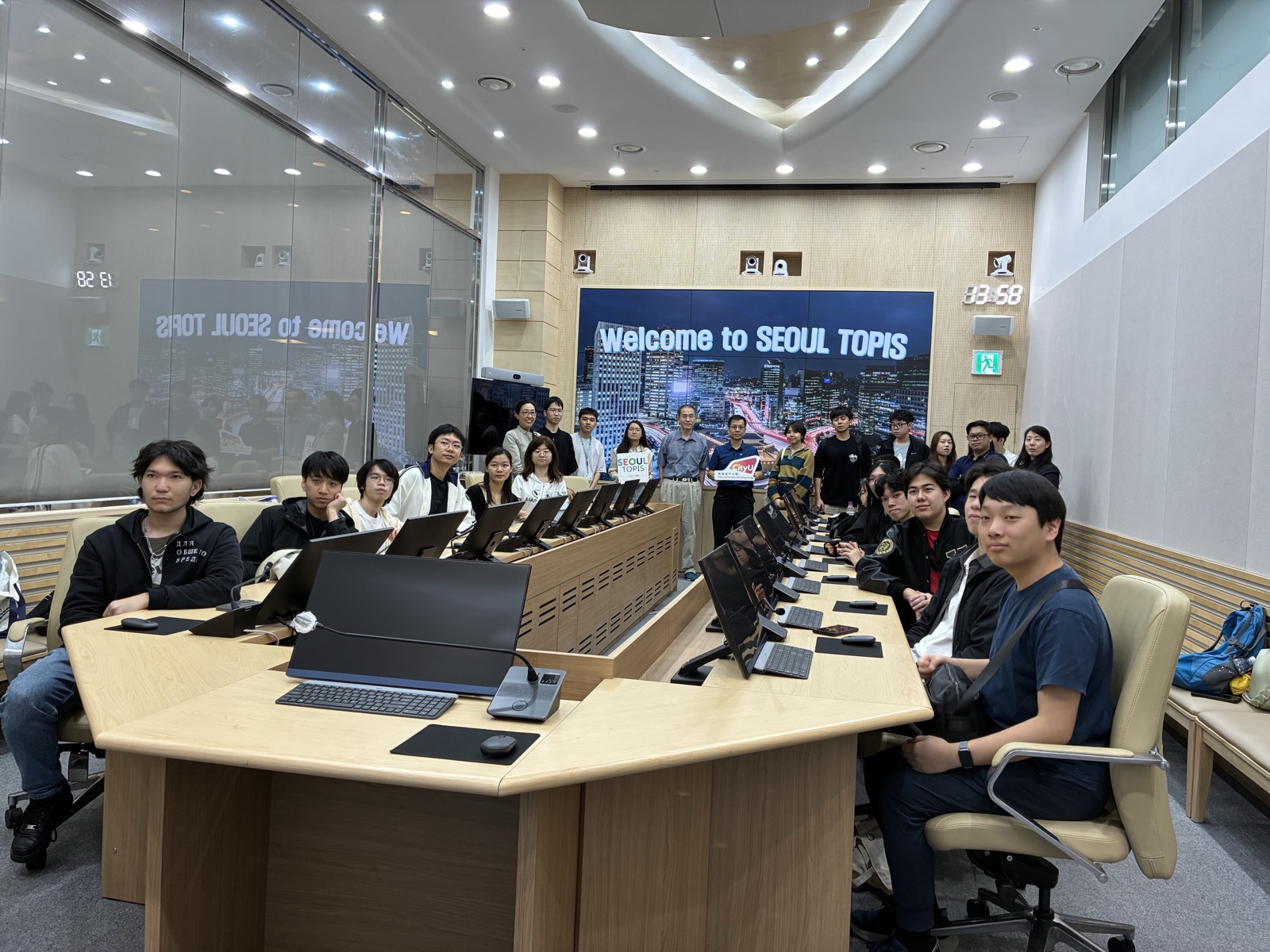 The whole group seated at terminals under a Welcome to SEOUL TOPIS screen