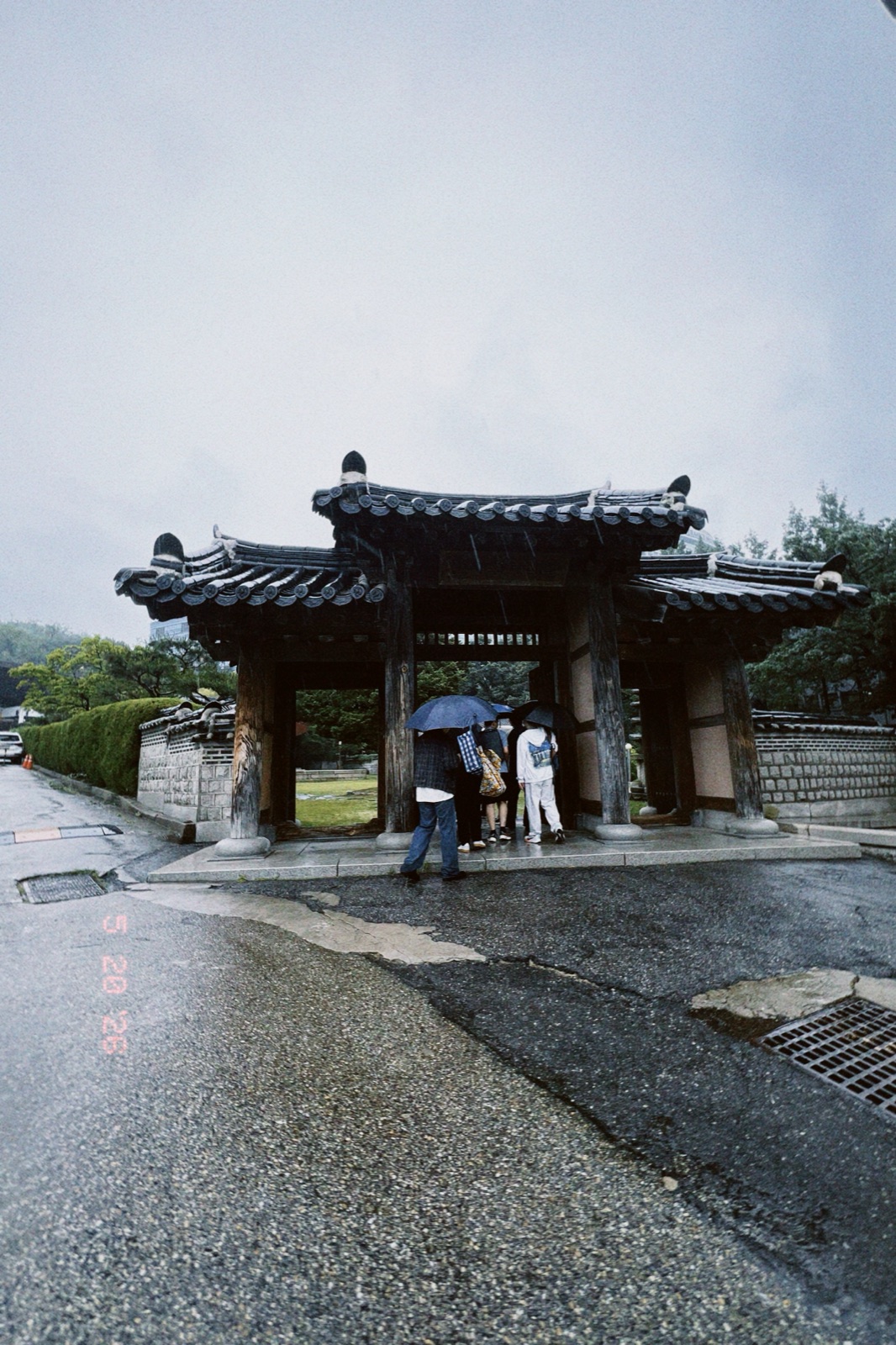 A traditional tiled-roof gate on campus, dark with rain